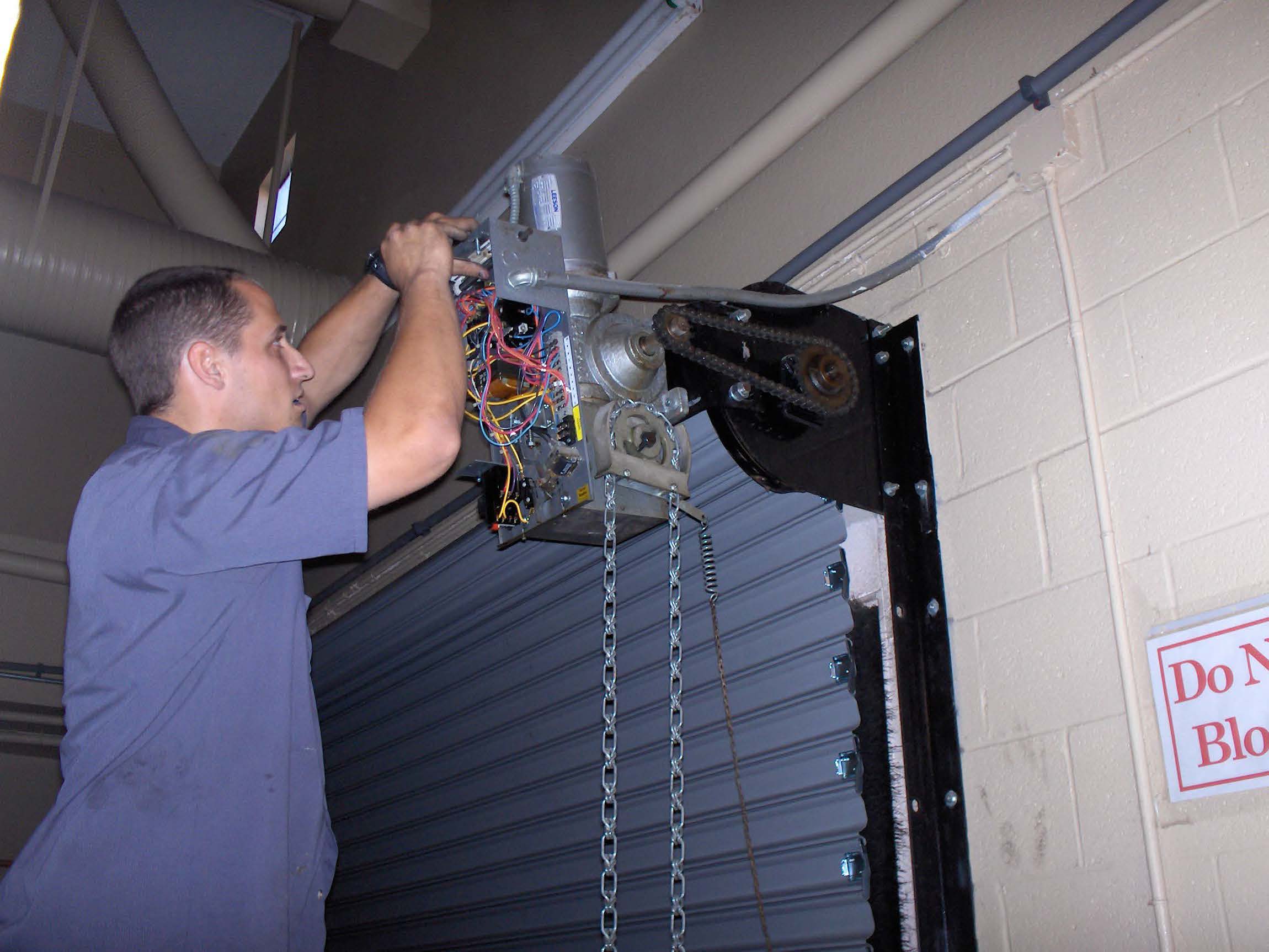 Technician repairing garage door motor, showcasing electrical components and chain mechanism, emphasizing reliability and service expertise of Day & Nite Doors Inc.